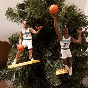 May include: Two basketball player ornaments hanging on a green Christmas tree. The ornaments are of Michael Jordan and Scottie Pippen, both wearing their Chicago Bulls uniforms. The ornaments are made of plastic and have a gold stand.