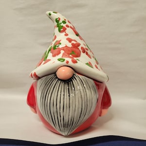 May include: A ceramic gnome figurine with a red and white hat with green and pink polka dots. The gnome has a white beard with black stripes and a red body.