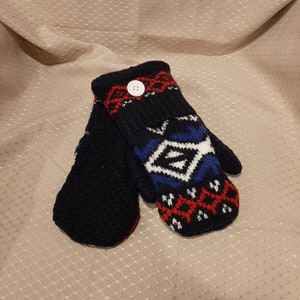 May include: A pair of black knit mittens with a white, blue, and red geometric pattern. One mitten has a white button.