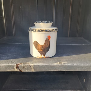 May include: White ceramic butter dish with a black rooster design. The dish has a black rim and a distressed white finish.
