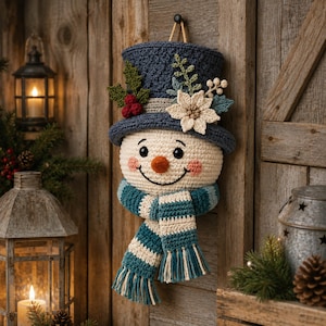 May include: A crocheted snowman wall hanging featuring a dark blue top hat adorned with a cream-colored poinsettia, green leaves, and red berries. The snowman has a round cream face, a small orange nose, and a striped teal and cream scarf with fringe.