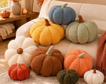 May include: A collection of nine plush pumpkin-shaped pillows in various sizes and colors, including blue, yellow, sage green, cream, brown, orange, dark red, dark green, and white, all featuring a textured, fuzzy fabric and a stem.