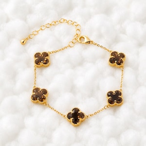 Puede incluir: Una pulsera de cadena en tono dorado con cinco dijes en forma de trébol de cuatro hojas espaciados uniformemente. Cada dije está incrustado con una piedra preciosa facetada de color marrón oscuro. Incluye una cadena fina y un cierre de mosquetón.