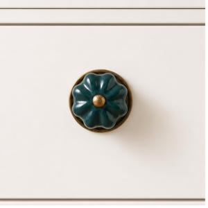 May include: A dark green, flower-shaped cabinet knob with a glossy finish and a central brass-toned metal accent. The knob is mounted on a circular brass-toned base and is attached to a flat, off-white surface with horizontal paneling.