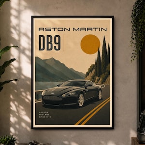 May include: A framed poster featuring a black Aston Martin DB9 driving on a coastal road. The artwork includes a yellow sun, mountains, and cypress trees. Text reads ASTON MARTIN DB9 and GAYDON ENGLAND SINCE 1913 in a clean, modern font style.