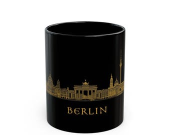May include: A black ceramic mug featuring a gold-colored line art illustration of the Berlin city skyline. The design includes iconic landmarks such as the Brandenburg Gate and the TV Tower, with the word BERLIN printed in gold below the skyline.