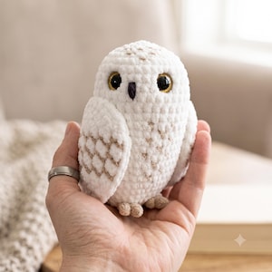 Peut inclure: Un petit hibou en peluche crocheté blanc avec une surface texturée en fil. Le hibou présente de grands yeux ronds et sombres avec des iris dorés, un petit bec noir et des accents brun clair sur ses ailes et ses pattes, conçu dans un style doux.