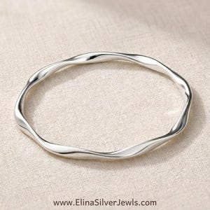 May include: A polished silver bangle bracelet featuring a continuous, smooth, undulating wave pattern throughout its circular band. The metal surface is reflective and metallic, with the text www.ElinaSilverJewels.com printed at the bottom.