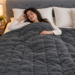 Könnte beinhalten: Eine dunkelgraue Gewichtsdecke mit einem quadratisch gesteppten Gittermuster. Die Decke hat eine plüschige, strukturierte Oberfläche und liegt auf einem Bett, wobei sie den unteren Teil mit ihrer dicken, gesteppten Konstruktion bedeckt.