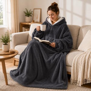 May include: A dark gray oversized hooded blanket sweatshirt featuring a thick, fuzzy texture, a large front pocket, and a white sherpa-lined hood. The garment is long, draping down to cover the legs, and includes long sleeves with ribbed cuffs.