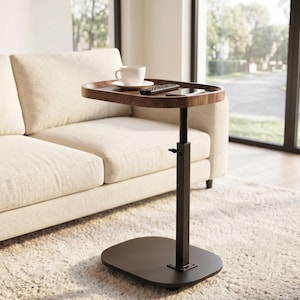 May include: A height-adjustable side table with a dark wood grain oval top and a black metal base. The tabletop holds a white ceramic mug on a saucer, a black remote control, and a smartphone. The table features a central vertical support column.
