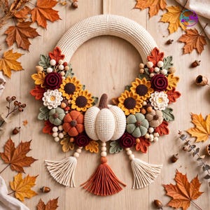 Puede incluir: Una corona de ganchillo circular con una calabaza color crema en el centro, rodeada de girasoles, rosas rojo oscuro, flores blancas y pequeñas calabazas en tonos verdes y naranjas. Tres borlas de hilo crema y naranja cuelgan debajo.