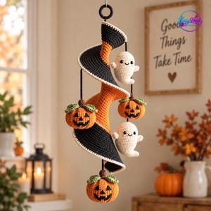 May include: A hanging crochet mobile featuring a central spiral structure in alternating black and orange yarn. Suspended from the spiral are two white crocheted ghosts with black eyes and smiles, and three orange crocheted pumpkins with green stems.