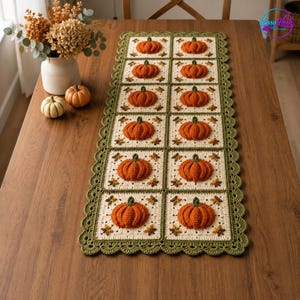 Pode incluir: Um caminho de mesa retangular de crochê com dez motivos quadrados, cada um exibindo um design de abóbora laranja em relevo sobre um fundo creme. O caminho tem uma borda festonada verde-oliva e pequenos motivos de folhas marrons.