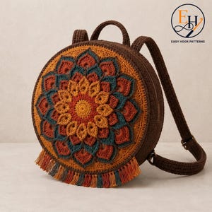 Könnte beinhalten: Ein runder Häkelrucksack in Dunkelbraun mit einem mehrschichtigen Mandalamuster auf der Vorderseite. Das Design umfasst konzentrische Ringe aus Blütenblättern in Senfgelb, Rostorange und Petrol. Eine Fransenborte säumt den unteren Rand.