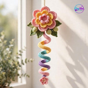May include: A hanging crochet decoration featuring a multi-layered flower in shades of pink and yellow with green leaves. Below the flower hangs a long, spiraling tail in pastel colors including yellow, blue, purple, and pink, ending in a small flower.