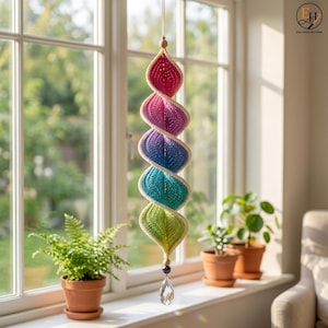 May include: A hanging spiral decoration made of crocheted yarn in a gradient of colors including pink, purple, blue, teal, and green. The spiral is suspended by a thin string and features a clear, faceted crystal pendant at the bottom.