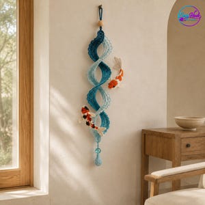 May include: A vertical crochet wall hanging featuring a spiraling blue and light blue wave pattern. Two crocheted koi fish, one orange and white and one black, white, and orange, are attached to the spiral. A wooden bead and blue crystal accent.