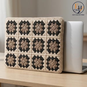 Puede incluir: Una funda rectangular para portátil con un patrón de ganchillo de cuadrados de la abuela en beige, marrón claro y gris carbón oscuro. La funda está construida con doce motivos cuadrados individuales dispuestos en una cuadrícula sobre un portátil.
