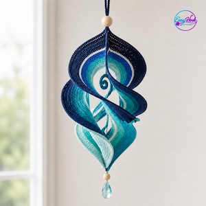 May include: A hanging spiral ornament crafted from crocheted yarn in a gradient of blue shades, ranging from dark navy to light turquoise. The structure features a wooden bead at the top and bottom, with a clear blue teardrop crystal at the base.