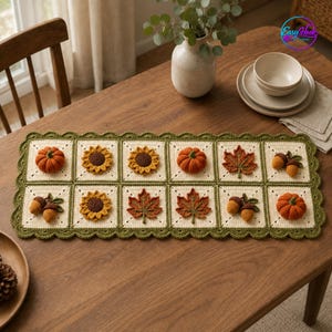 May include: A rectangular crochet table runner featuring ten square panels with cream-colored backgrounds and a dark green scalloped border. Each square displays a three-dimensional autumn-themed motif, including orange pumpkins, yellow sunflowers, brown acorns, and orange maple leaves.
