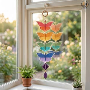 May include: A vertical hanging decoration featuring five crocheted butterflies in a gradient of colors including pink, orange, yellow, green, blue, and purple, suspended from a wooden ring with small wooden beads between each butterfly.
