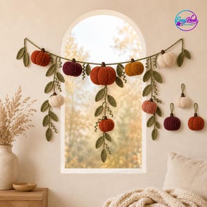 May include: A crochet garland featuring various pumpkins in shades of orange, burgundy, and cream, accented with green crocheted leaves and vines. The garland is displayed in a swag pattern, with additional individual pumpkin ornaments nearby.