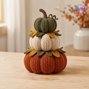 May include: A stacked crochet pumpkin decoration featuring three pumpkins in descending size order. The top is dark green, the middle is cream, and the bottom is orange. Each pumpkin is separated by a ring of crocheted green and yellow leaves.