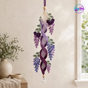 May include: A hanging crochet decoration featuring a central spiral structure in shades of cream, lavender, and deep purple, adorned with clusters of purple wisteria flowers and green leaves. A wooden bead and a clear crystal hang at the bottom.