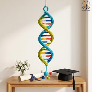 May include: A crocheted DNA double helix model hanging vertically, featuring vibrant blue, yellow, red, and white yarn segments. The structure is suspended from a loop at the top and terminates in a small, multi-colored crocheted molecular cluster.