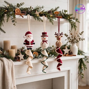 Pode incluir: Três ornamentos de crochê pendurados representando o Papai Noel, um boneco de neve com chapéu vermelho e uma rena. Cada figura está presa a uma longa cauda em espiral semelhante a tecido nas cores creme, verde ou vermelho.