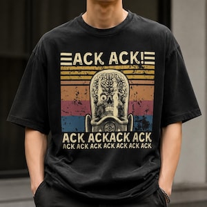 May include: A black short-sleeve t-shirt featuring a graphic of a Martian skull with an exposed brain inside a glass helmet. The design includes a retro sunset background with horizontal stripes and the text ACK ACK! ACK ACKACK ACK ACK.