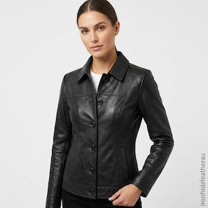 May include: A black leather jacket featuring a classic collar, long sleeves, and a front button-down closure with five visible buttons. The jacket has structured paneling, vertical seams, and two side pockets, worn over a plain white shirt.