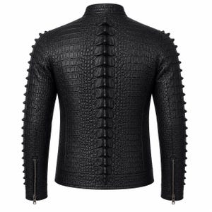 Puede incluir: Una chaqueta negra con un patrón texturizado de piel de cocodrilo, que presenta una hilera prominente de púas elevadas a lo largo del centro de la espalda y el borde exterior de cada manga, con puños con cremallera y cuello mao.