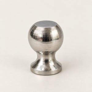 Op de afbeelding: Een bolvormige meubelknop van metaal met een gepolijste zilveren afwerking. De knop heeft een gladde, ronde bovenkant en een uitlopende, ronde voet die naar het midden toe taps toeloopt, wat een functioneel meubelonderdeel vormt.