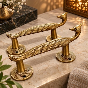 May include: Two brass door handles shaped like peacocks with detailed feather engravings along the body. Each handle features a long, curved neck and head at one end, supported by two circular mounting plates with a spiral pattern and screw holes.
