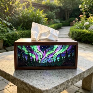 May include: A rectangular wooden tissue box cover featuring a stained glass panel on the front. The glass depicts a vibrant aurora borealis in shades of green and purple above a dark silhouette of pine trees against a starry night sky.
