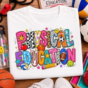 May include: A white t-shirt featuring a colorful graphic with the text PHYSICAL EDUCATION. The design includes various sports balls, a pencil, an apple, and stars in patterns like leopard print, checkers, and polka dots, arranged in two rows.