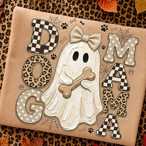 May include: A tan sweatshirt featuring the text DOG MAMA in varied patterns including black and white checkerboard, leopard print, and beige polka dots. A white ghost with a beige bow holds a bone, surrounded by spiderwebs and paw prints.