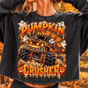Peut inclure: Un sweat-shirt gris anthracite à manches longues avec un motif de monster truck à calandre citrouille, entouré de fantômes et de citrouilles. Le texte PUMPKIN CRUSHER est imprimé dans une police orange et jaune dégoulinante.