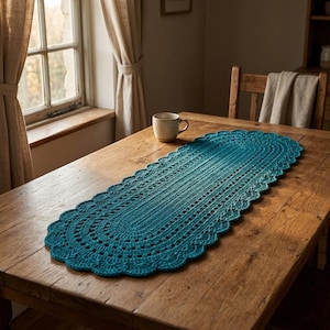 May include: An oval-shaped teal crochet table runner featuring a textured, intricate stitch pattern with a scalloped edge. The runner is crafted from yarn and displays a consistent deep blue-green colour throughout its elongated, decorative design.