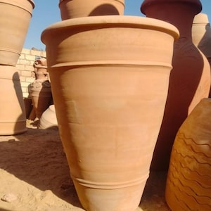 Peut inclure: Une collection de grands pots et récipients en terre cuite non émaillée, dotés de corps lisses et coniques avec des bandes horizontales en relief. Les pots présentent une finition en argile brun-rouge naturel sous un ciel bleu clair.