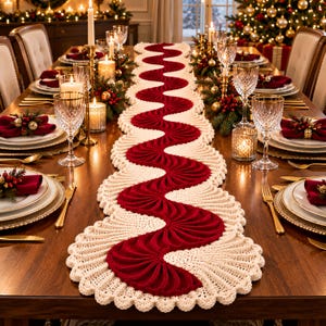 May include: A long, wavy table runner featuring a central deep red crocheted section with a fan-like texture, bordered by a wide, cream-colored crocheted edge with a scalloped trim, laid flat down the center of a wooden dining table.