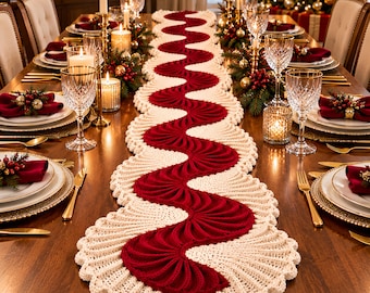 May include: A long, wavy table runner featuring a central deep red crocheted section with a fan-like texture, bordered by a wide, cream-colored crocheted edge with a scalloped trim, laid flat down the center of a wooden dining table.