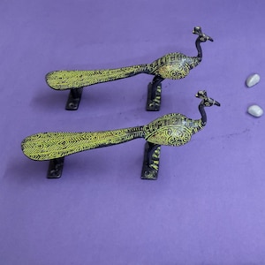 May include: Two matching metal door handles shaped like peacocks, featuring a dark black base color with bright yellow etched patterns on the bodies and long tails. Each handle has two rectangular mounting plates for attachment to a door surface.