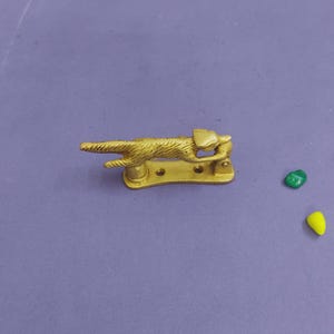 May include: A gold-colored metal door knocker shaped like a running fox. The fox is depicted in a horizontal, leaping position with textured fur details. The base of the knocker is a flat, curved metal plate with two visible screw holes for mounting.