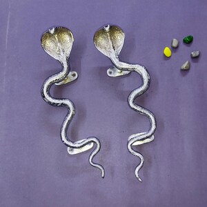 May include: Two silver-toned metal door handles shaped like upright cobras with flared hoods and winding bodies. Each handle features intricate engraved patterns on the hood and a mounting plate with two screw holes for secure installation.