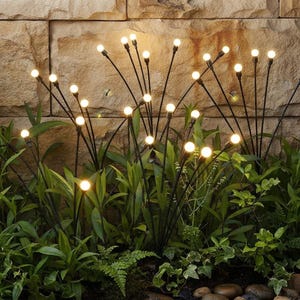 May include: A set of outdoor garden lights featuring multiple thin black metal stems topped with glowing warm white spherical bulbs. The lights are arranged in clusters among green foliage, creating an effect of fireflies in a garden setting.