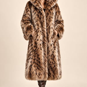 May include: A long, hooded coat featuring a brown and tan faux fur texture with a dark brown spotted animal print pattern. The coat has long sleeves, a large hood, and a straight-cut silhouette that reaches below the knees.
