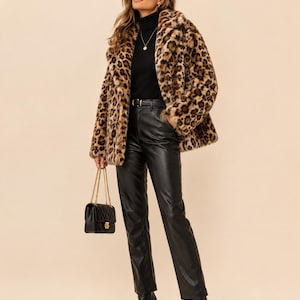 May include: A leopard print faux fur coat with a wide collar, worn over a black turtleneck sweater and black leather trousers. The outfit includes a small black quilted handbag with a gold chain strap and black pointed-toe ankle boots.
